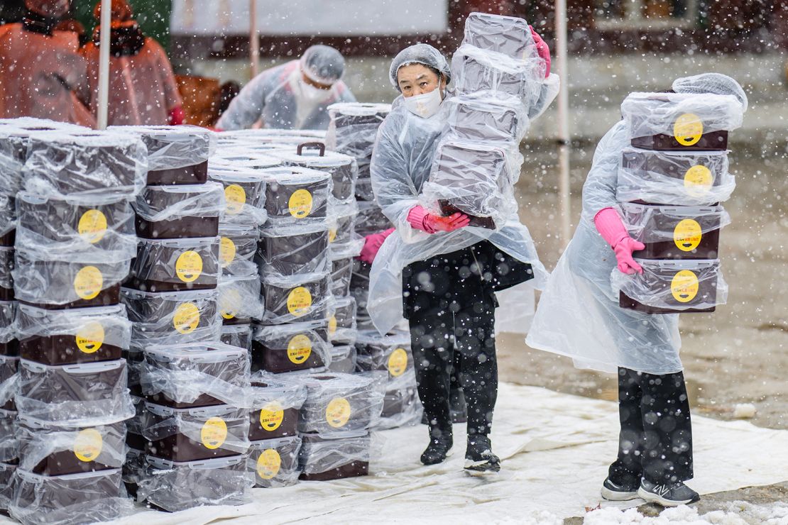 Participants carry boxes of freshly made kimchi during a kimchi-making festival at Jogyesa Temple in Seoul, held amid snowfall.